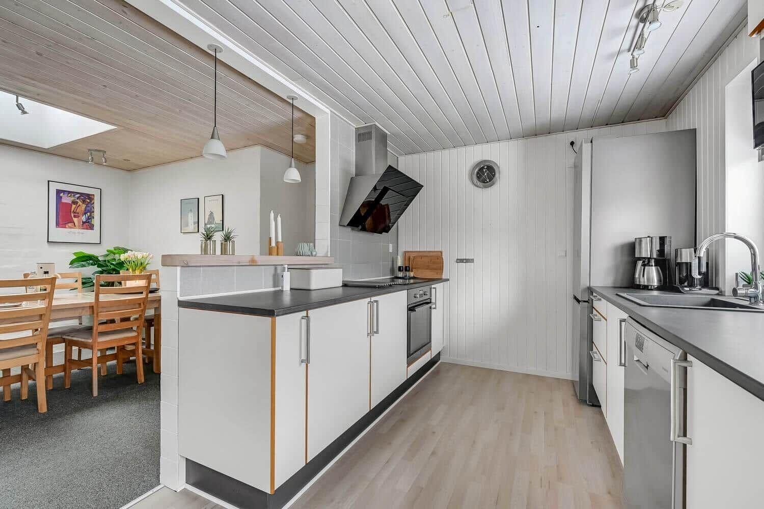Kitchen with dining area, white cabinets, and wooden floor. Countertop, sink, and stove are present.