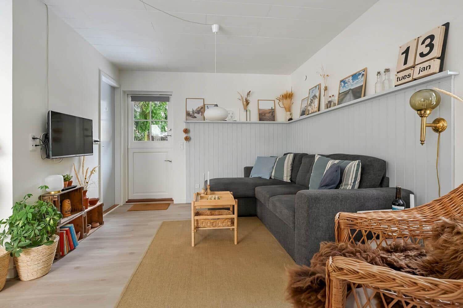 Wohnzimmer mit grauem Sofa, Holztisch und Wandregal mit Bildern.