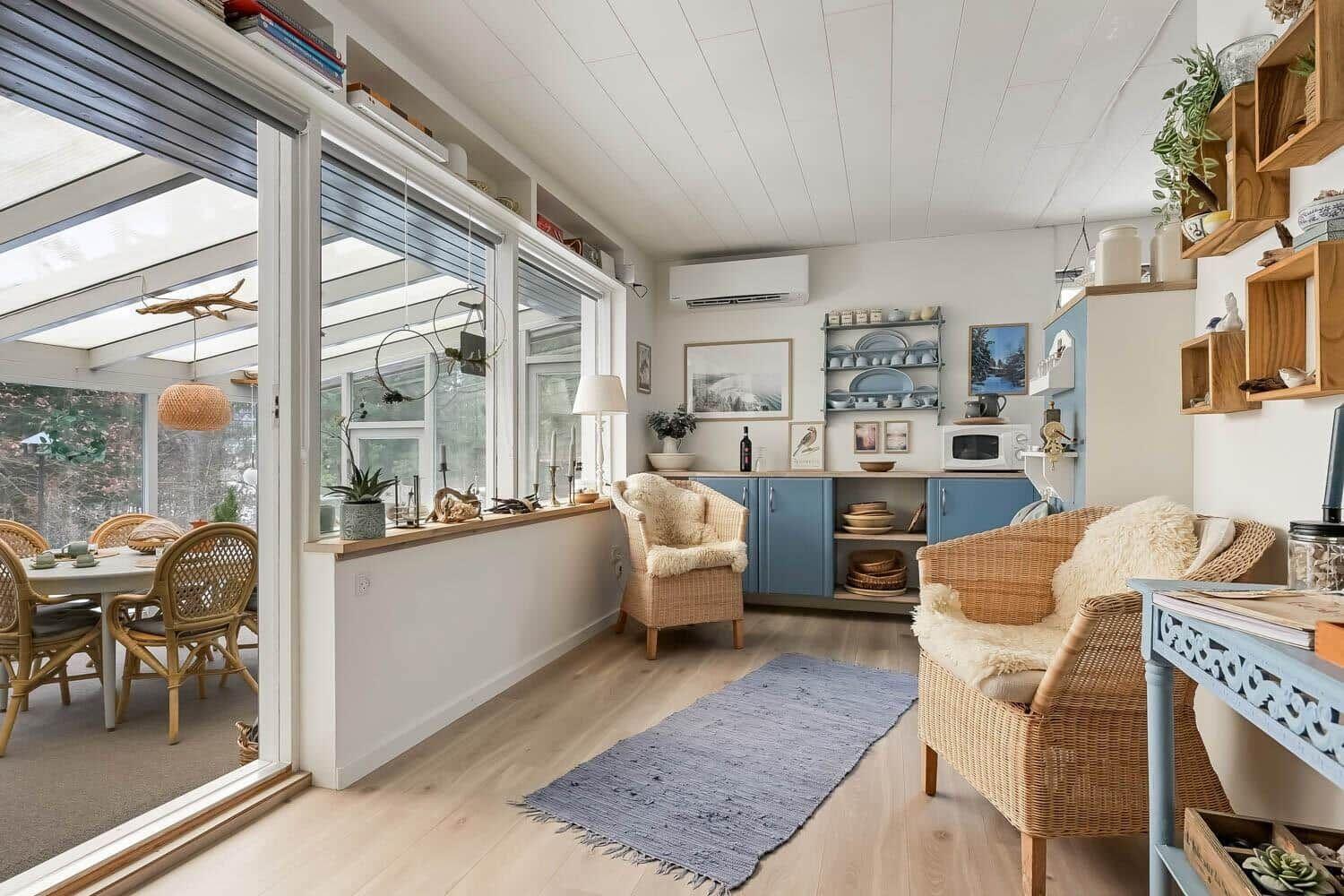 Wohnbereich mit Essbereich, blauen Schränken und Rattanmöbeln. Fenster zur Terrasse.