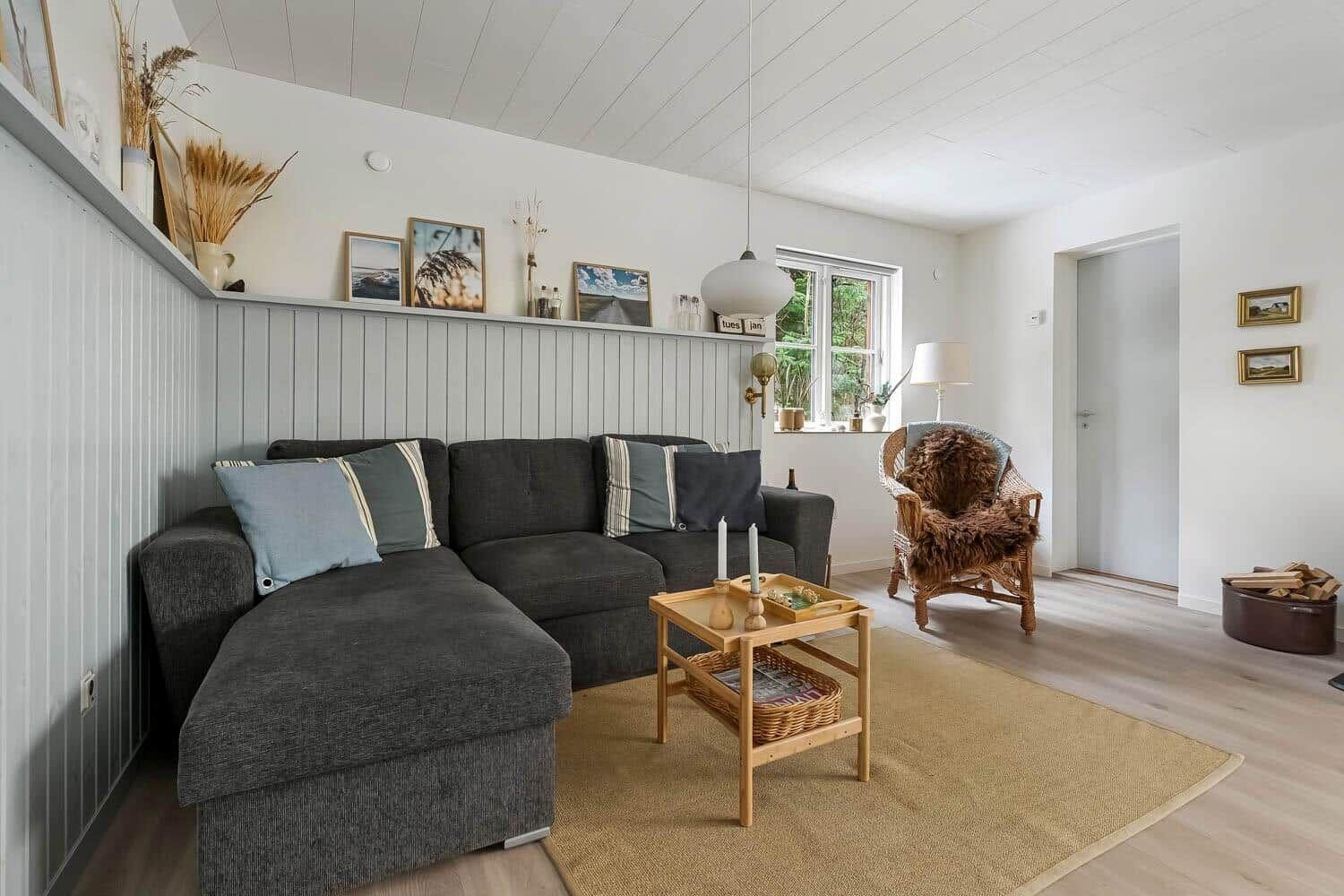 Ein Wohnzimmer mit grauem Sofa, Holztisch und Sessel. An der Wand hängen Bilder und Dekorationsgegenstände.