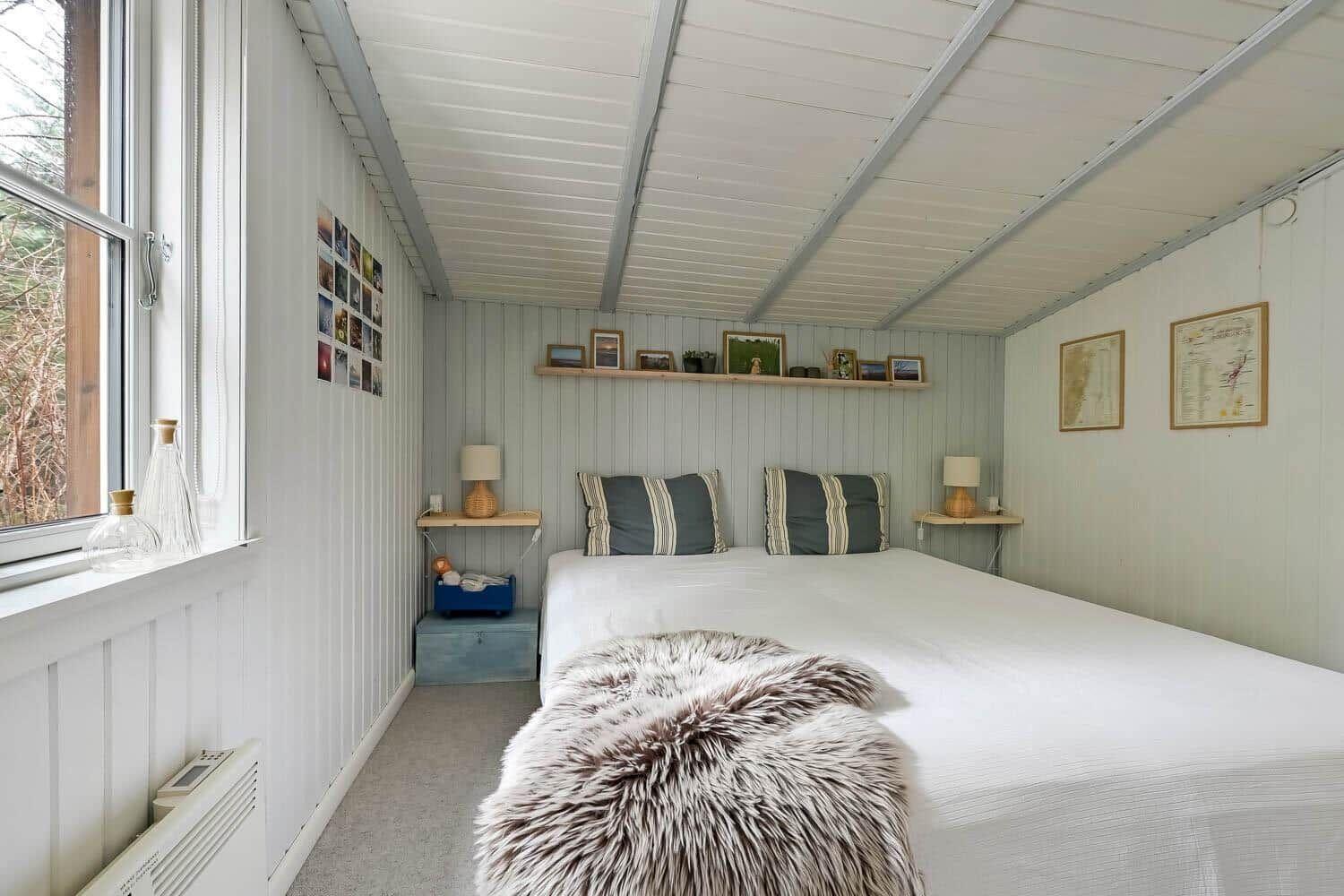 Ein Schlafzimmer mit einem Bett, zwei Nachttischen, einem Fenster und einer Decke.