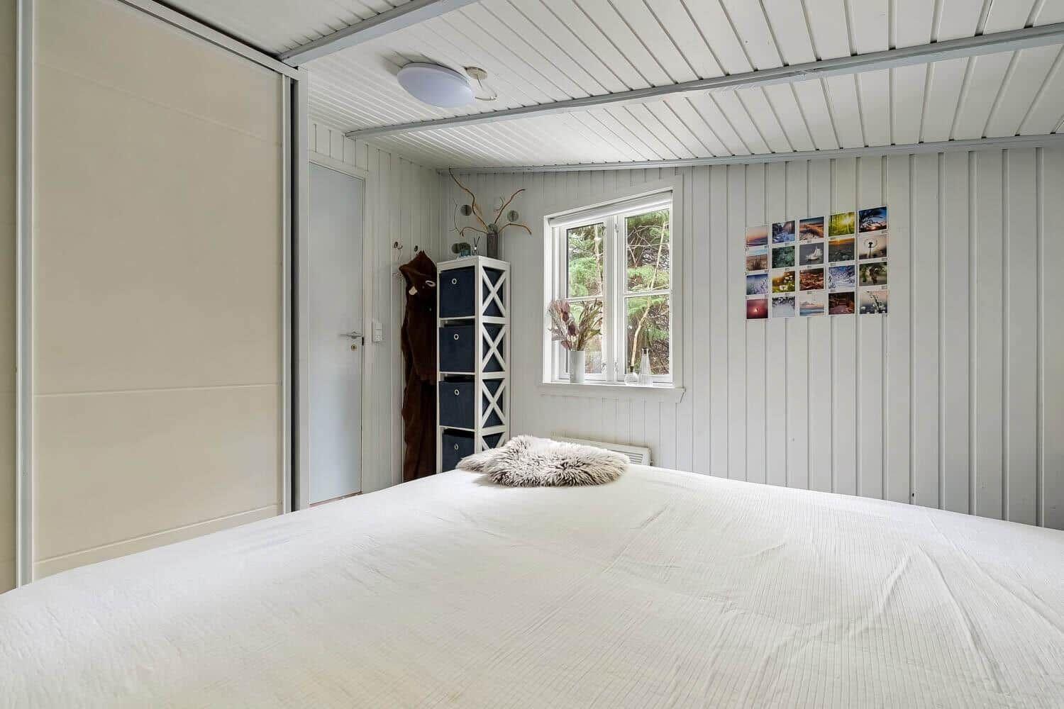 Schlafzimmer mit großem Bett, Fenster und weißen Wänden. An der Wand hängt eine Fotowand.