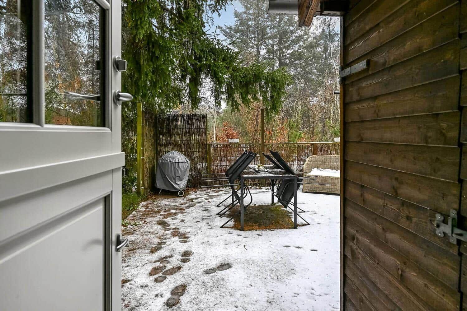 Von der Tür blickt man auf eine schneebedeckte Terrasse mit Tisch, Stühlen und Gartenmöbeln.