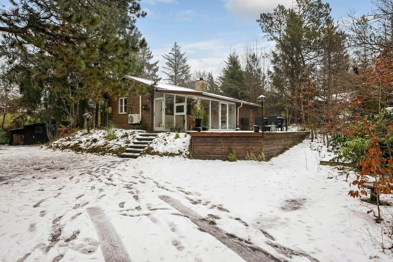 Holzhaus mit Glasfront und Terrasse im Schnee, umgeben von Bäumen.