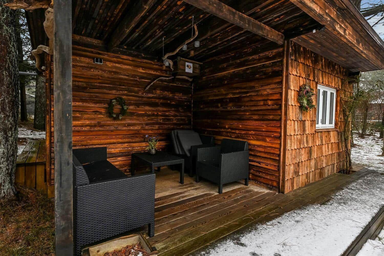 Holzveranda mit Sitzgruppe und Fenster. Schnee liegt auf dem Boden.