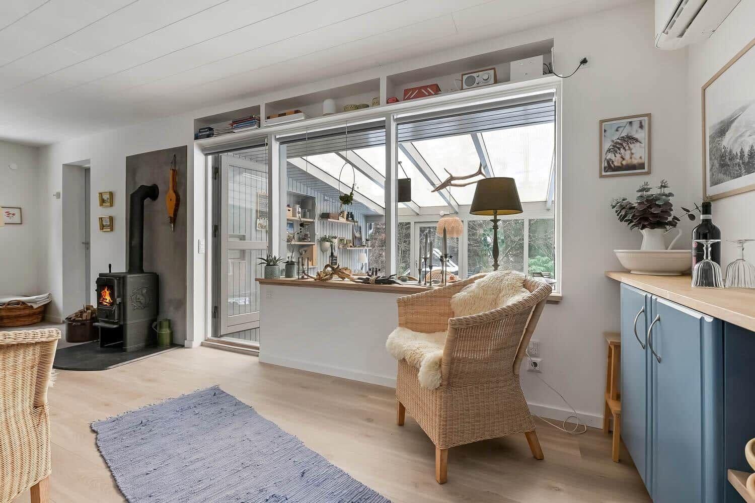 Wohnbereich mit Holzboden, Kamin und Sitzgelegenheit vor großem Fenster.