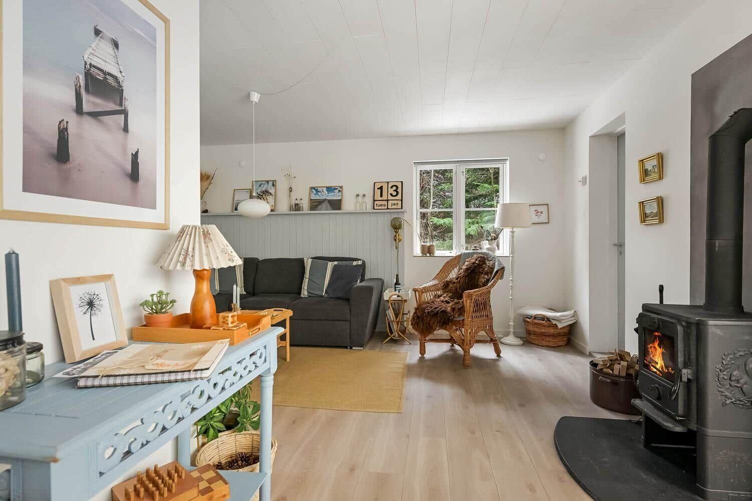 Wohnzimmer mit Sofa, Stuhl und Kamin. Holzboden und Fenster mit Blick auf Wald.