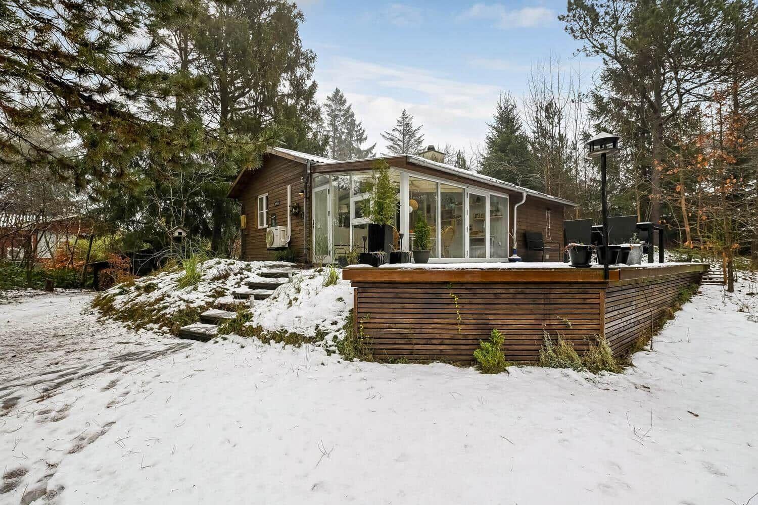 Holzhaus mit Glasfront und Terrasse im Schnee, umgeben von Bäumen.