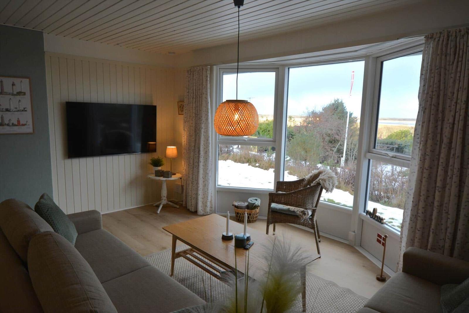 Wohnzimmer mit Sofa, Couchtisch und großem Fensterblick auf Schneelandschaft.