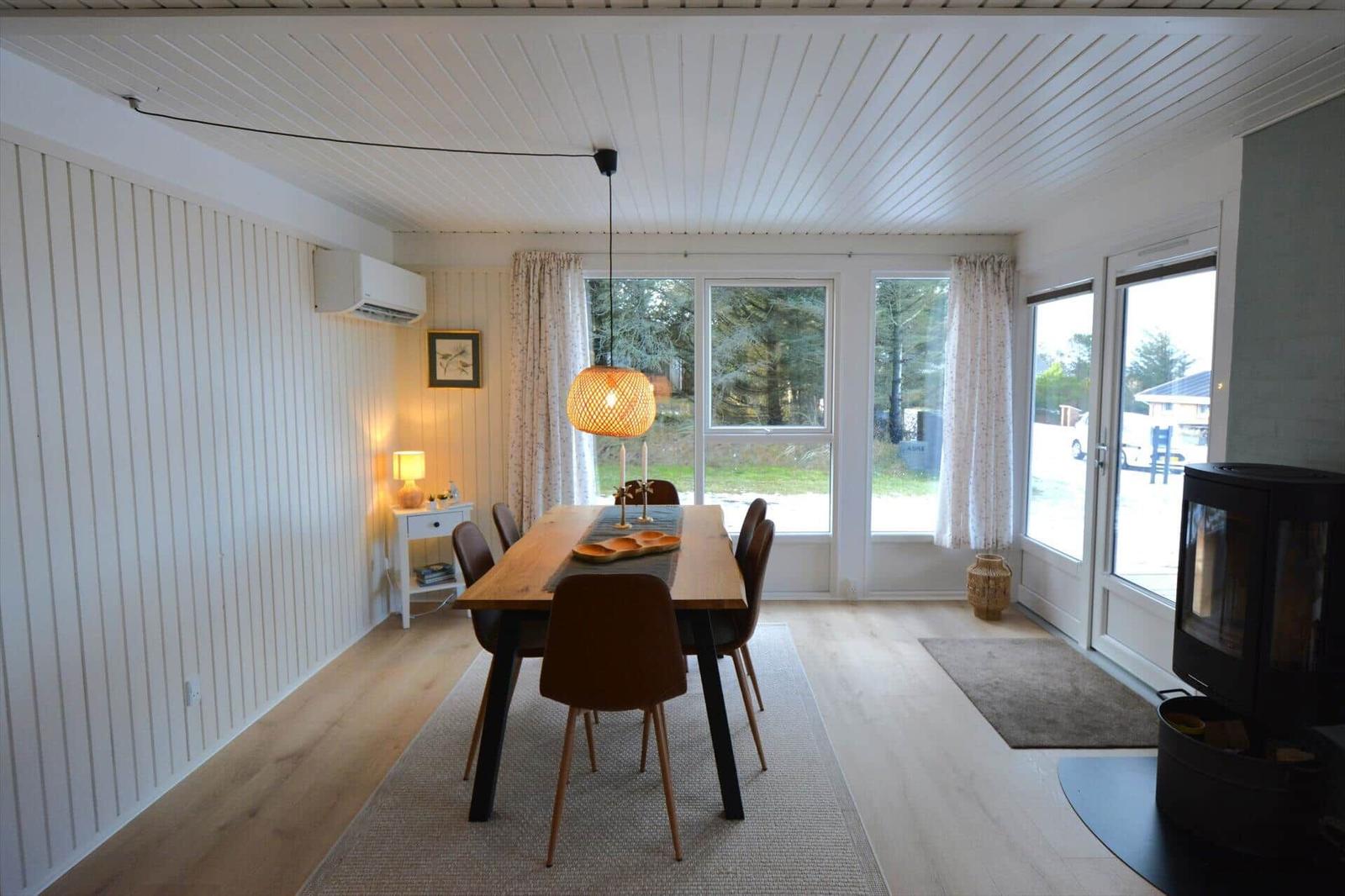 Esszimmer mit Holztisch, Stühlen und Fenstern zum Garten. Kamin und Deckenleuchte sichtbar.
