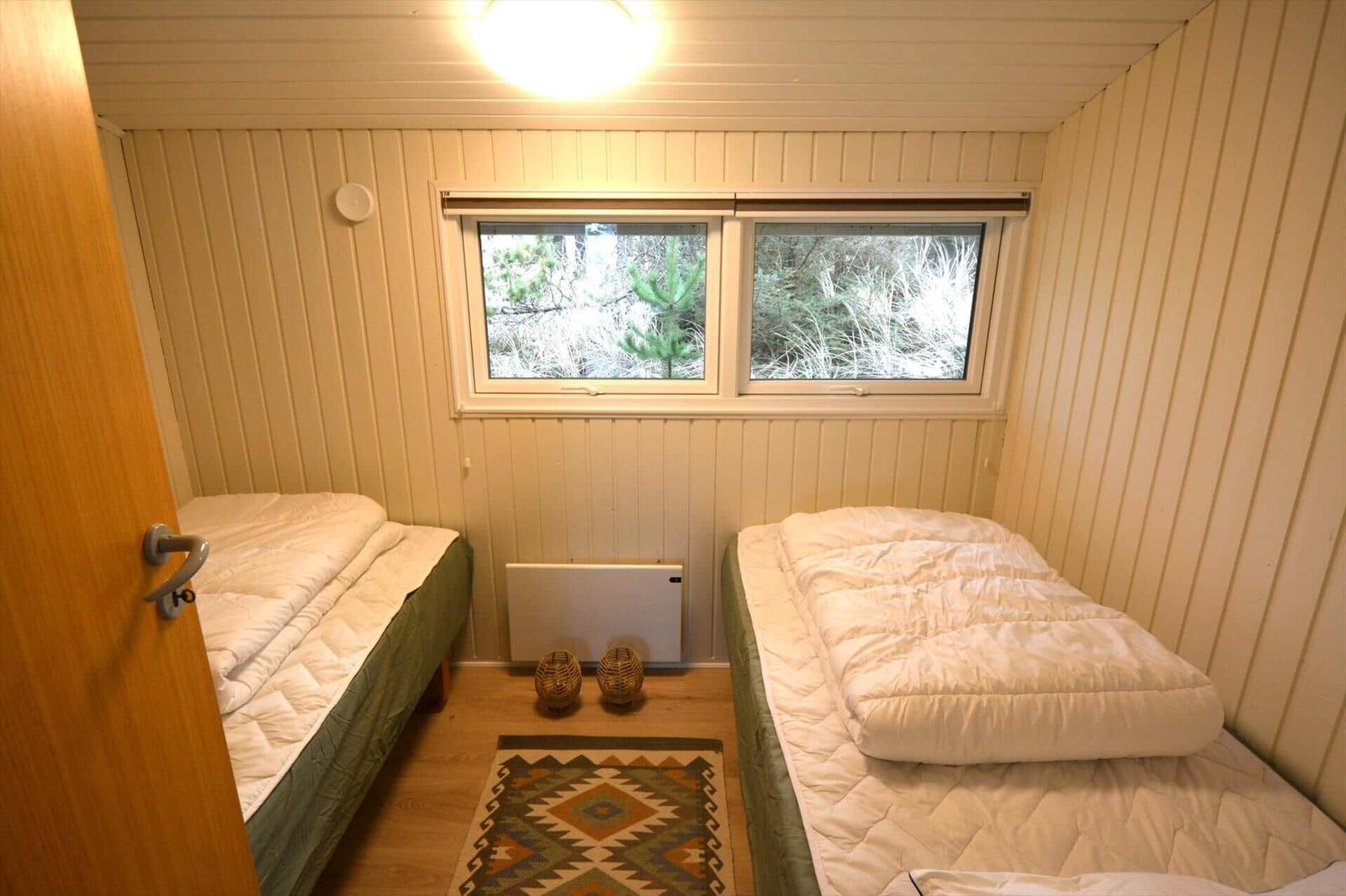 Zwei Betten mit weißen Decken, Holzwand und Fenster mit Blick auf Wald.