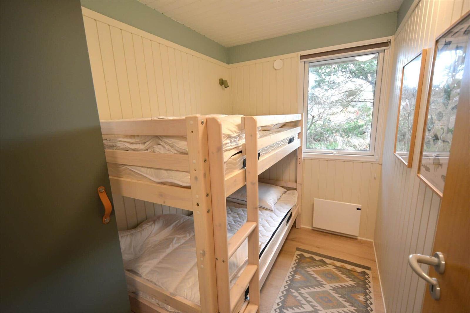 Zimmer mit Doppelstockbett, Fenster und Holzwandverkleidung.