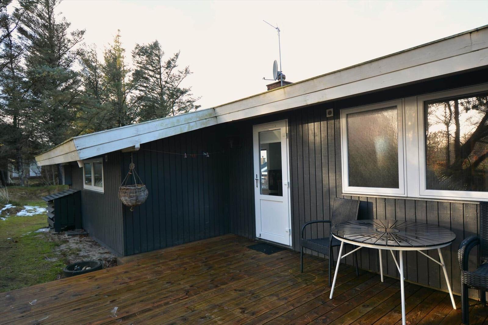 Haus mit Terrasse, Tisch und Stühlen, umgeben von Bäumen.