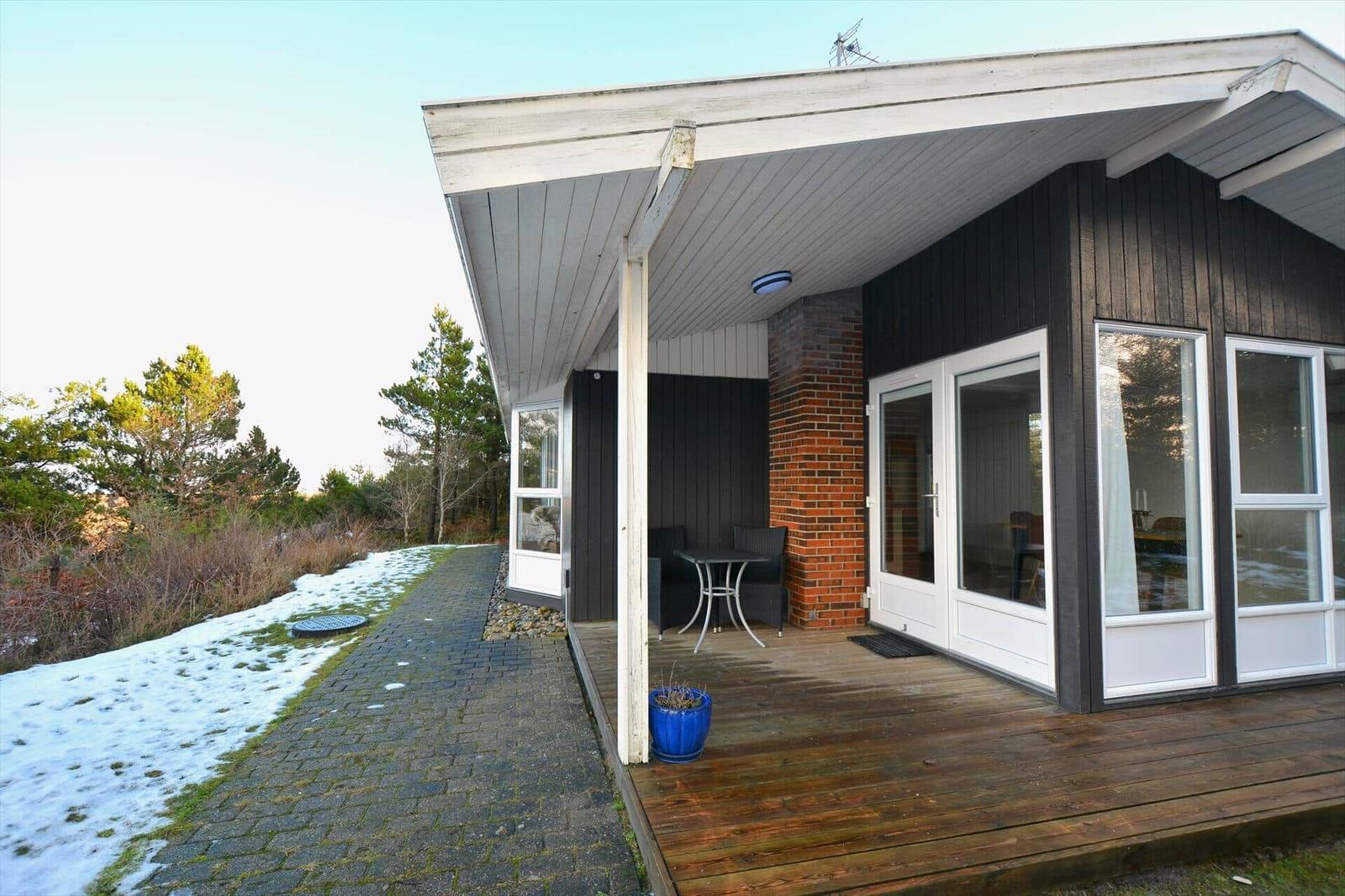 Haus mit Terrasse, Tisch und Stühlen. Schnee bedeckt den Boden. Holzterrasse und Fensterfront.