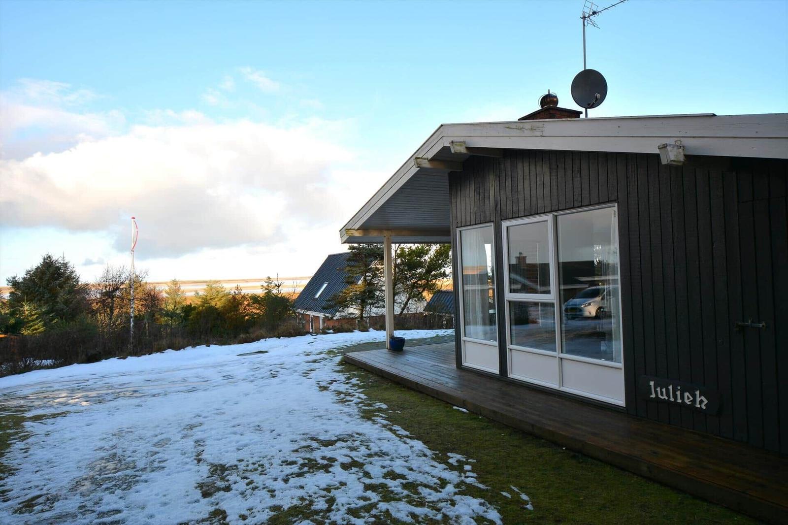 Ein dunkelholzverkleidetes Haus mit Glasfront und schneebedecktem Grundstück.