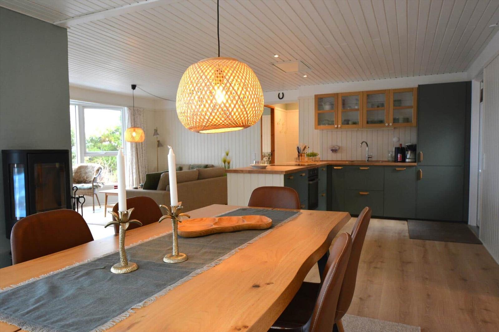 Essbereich mit Holztisch, Stühlen und Lampe. Küche mit grünen Schränken und Arbeitsplatte.