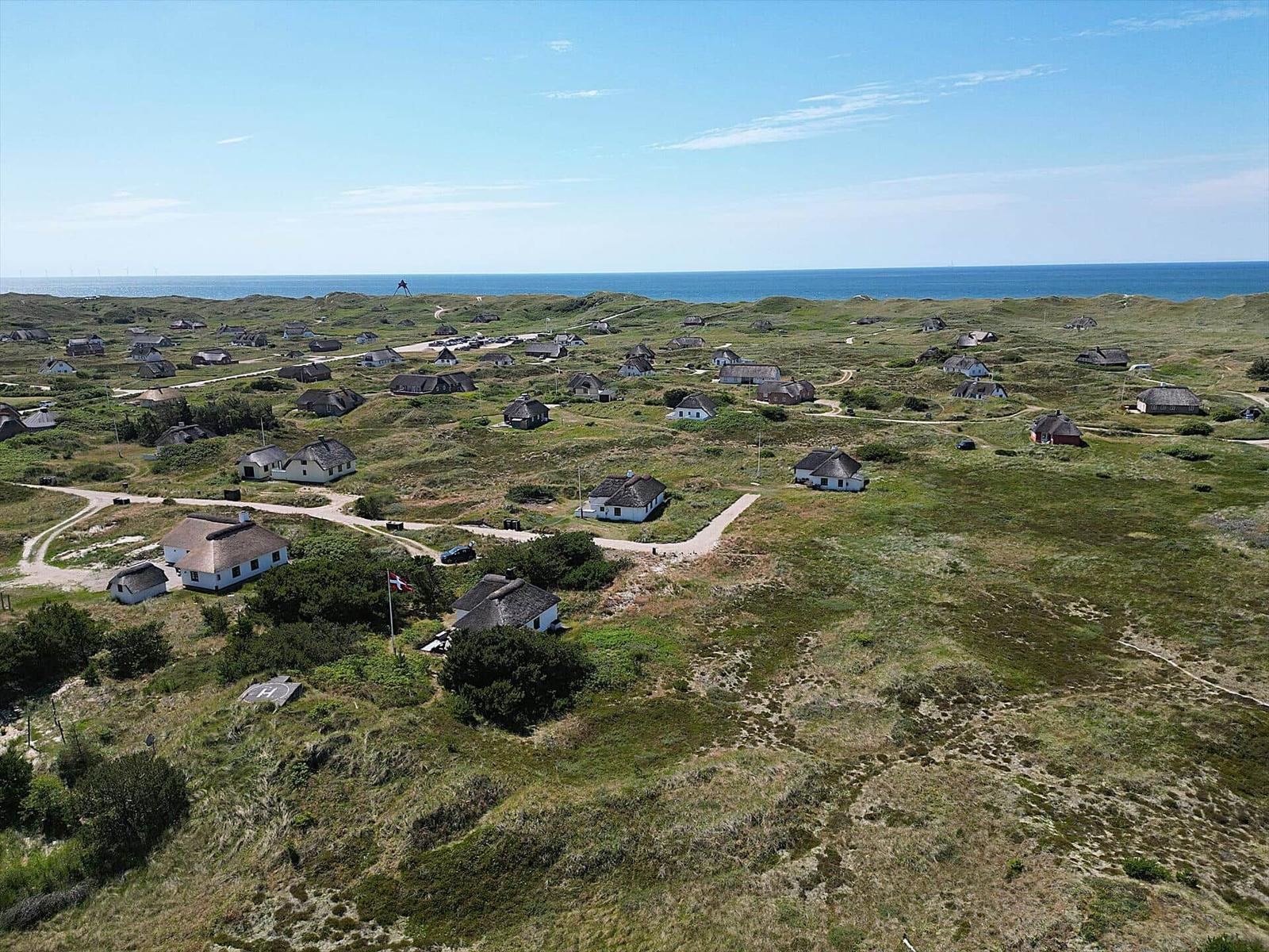 Dorf mit strohgedeckten Häusern auf grüner Dünenlandschaft, Blick auf das Meer.