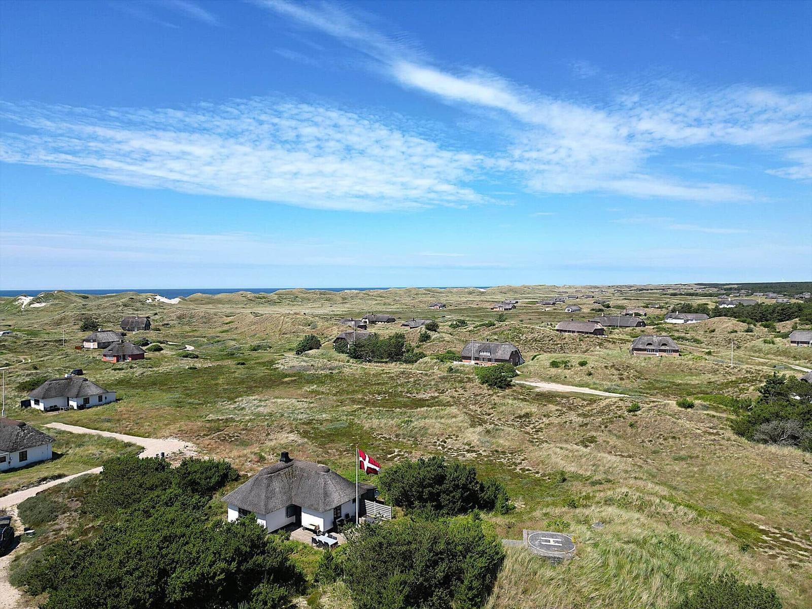 Dorf mit strohgedeckten Häusern auf Dünen, Blick auf Nordsee unter blauem Himmel.