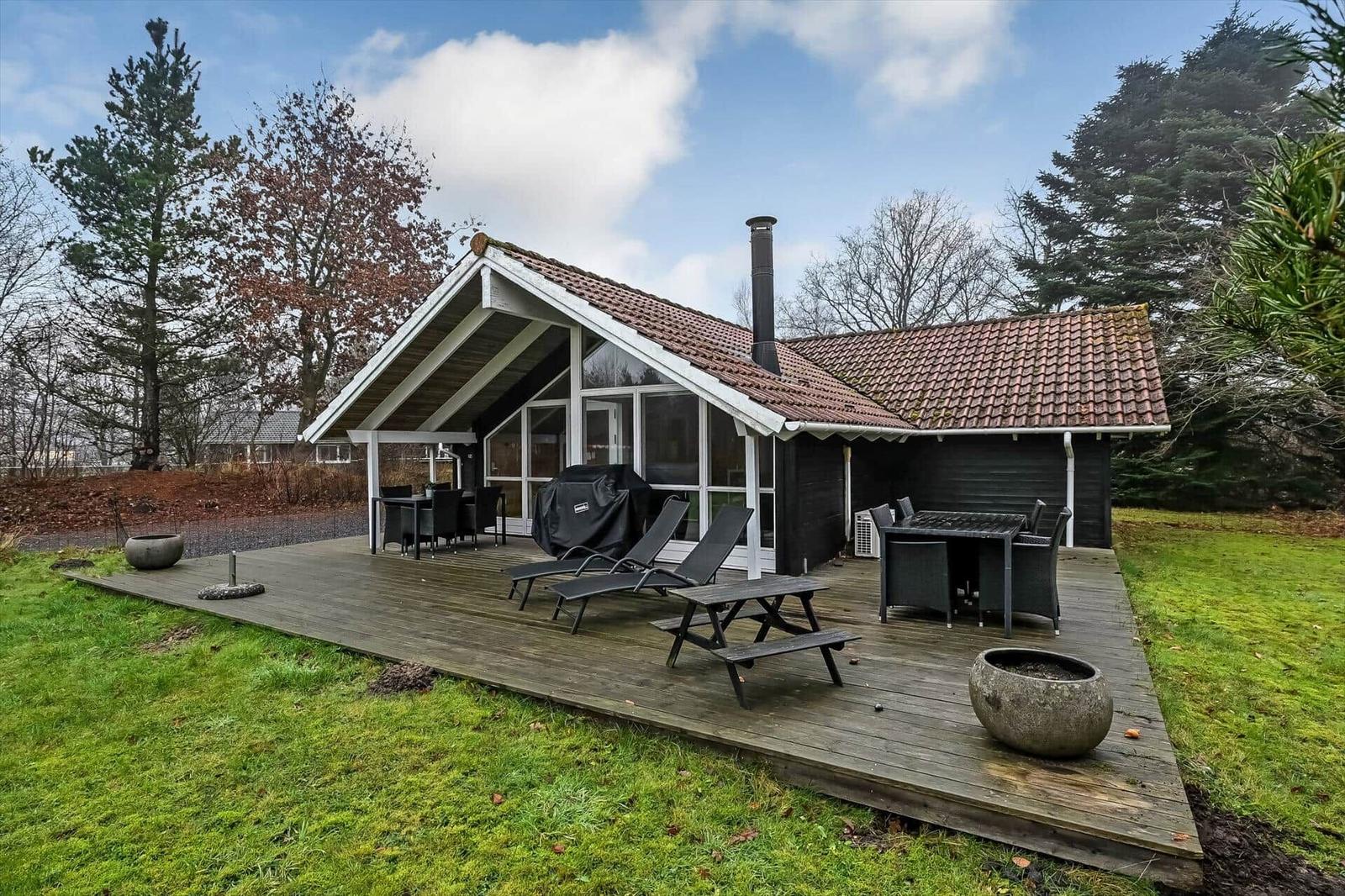 Haus mit Holzterrasse, Grill, Liegen und Tischen im Garten.