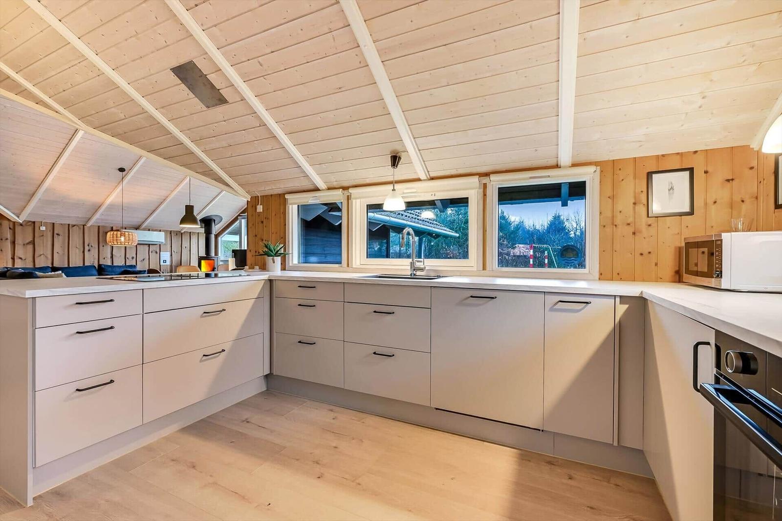 Küche mit Holzdecke, Fenstern und modernen Schränken.