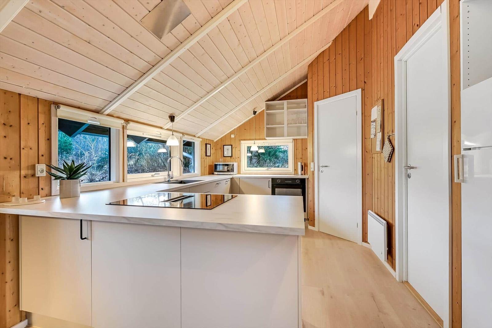 Küche mit Holzwand, Arbeitsplatte und Fenstern zum Wald