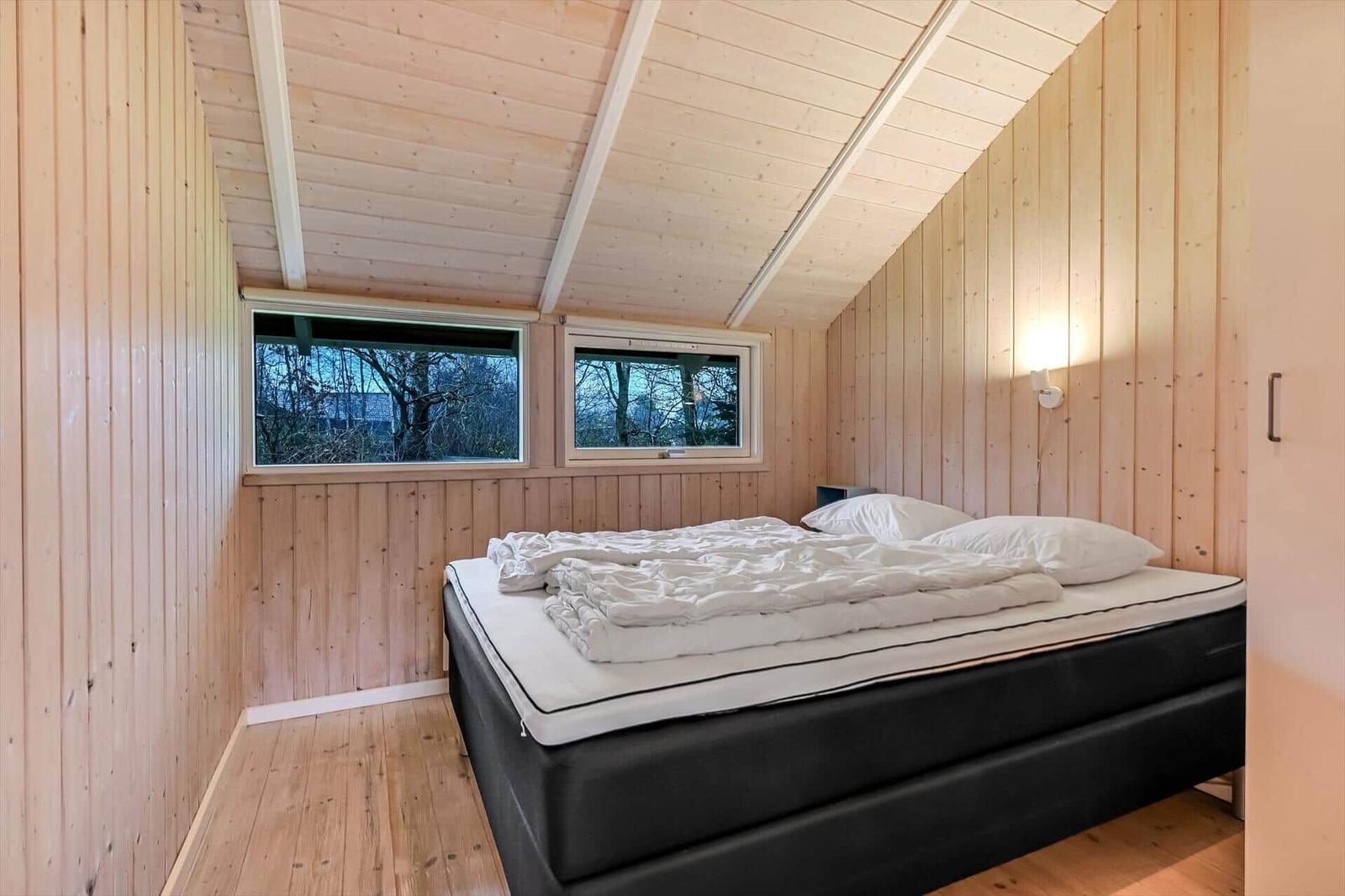 Schlafzimmer mit Holzwänden, Doppelbett und zwei Fenstern zur Aussicht.