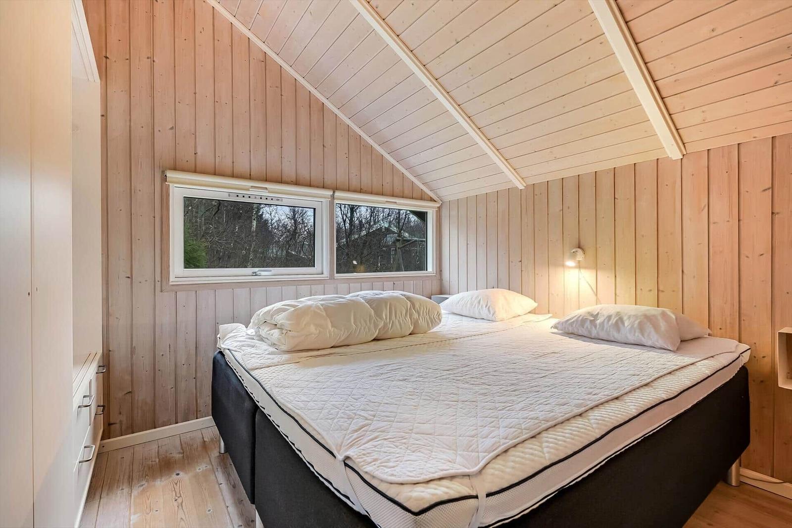 Schlafzimmer mit Holzwand und Dachfenster, Bett mit weißer Bettwäsche.