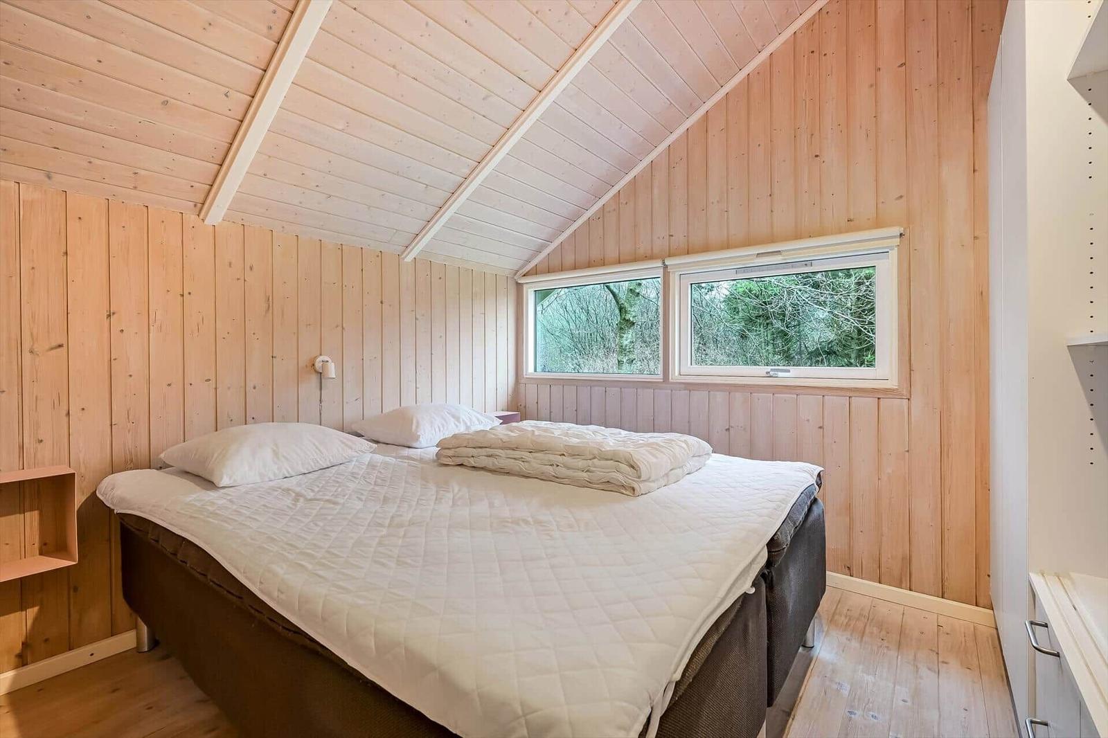 Schlafzimmer mit Holzwand, Bett und Fenster zum Wald
