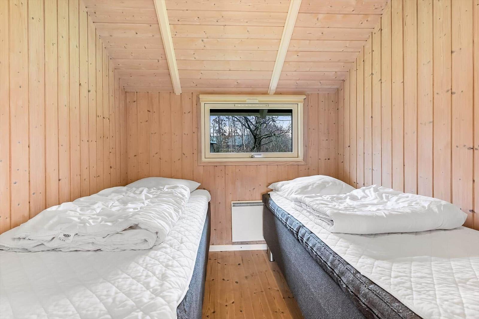 Zwei Einzelbetten in einem holzverkleideten Raum mit Fenster und Heizkörper.