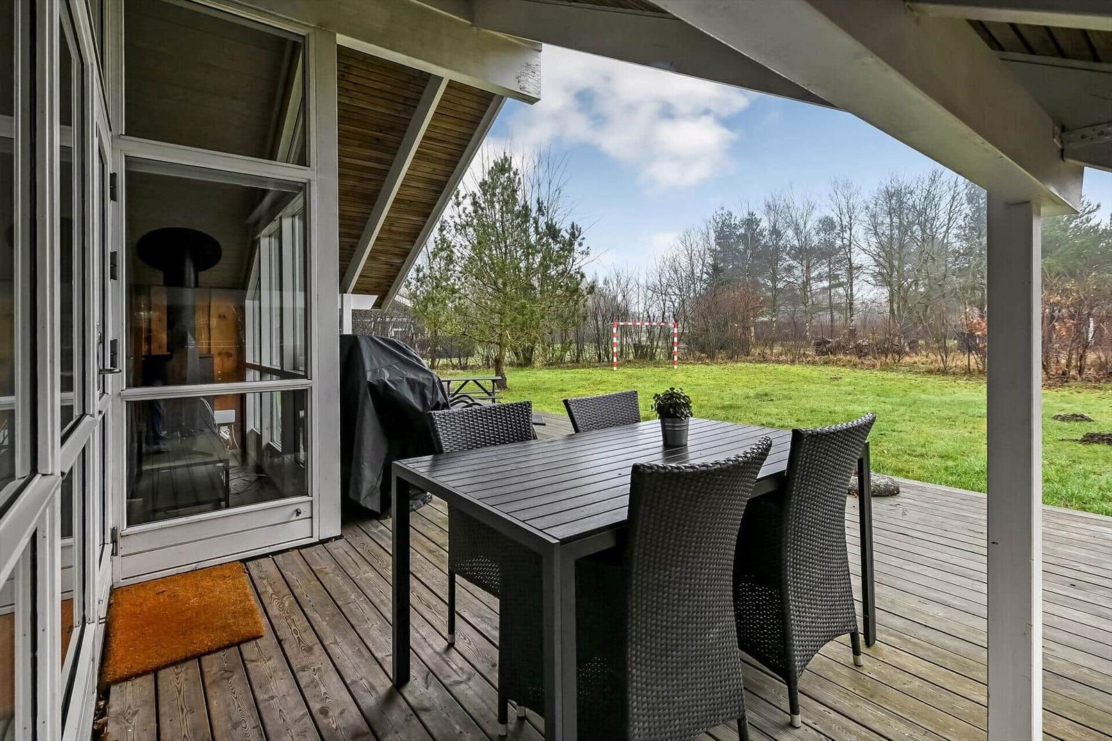 Terrasse mit Tisch und Stühlen, Blick auf grünen Rasen und Bäume.