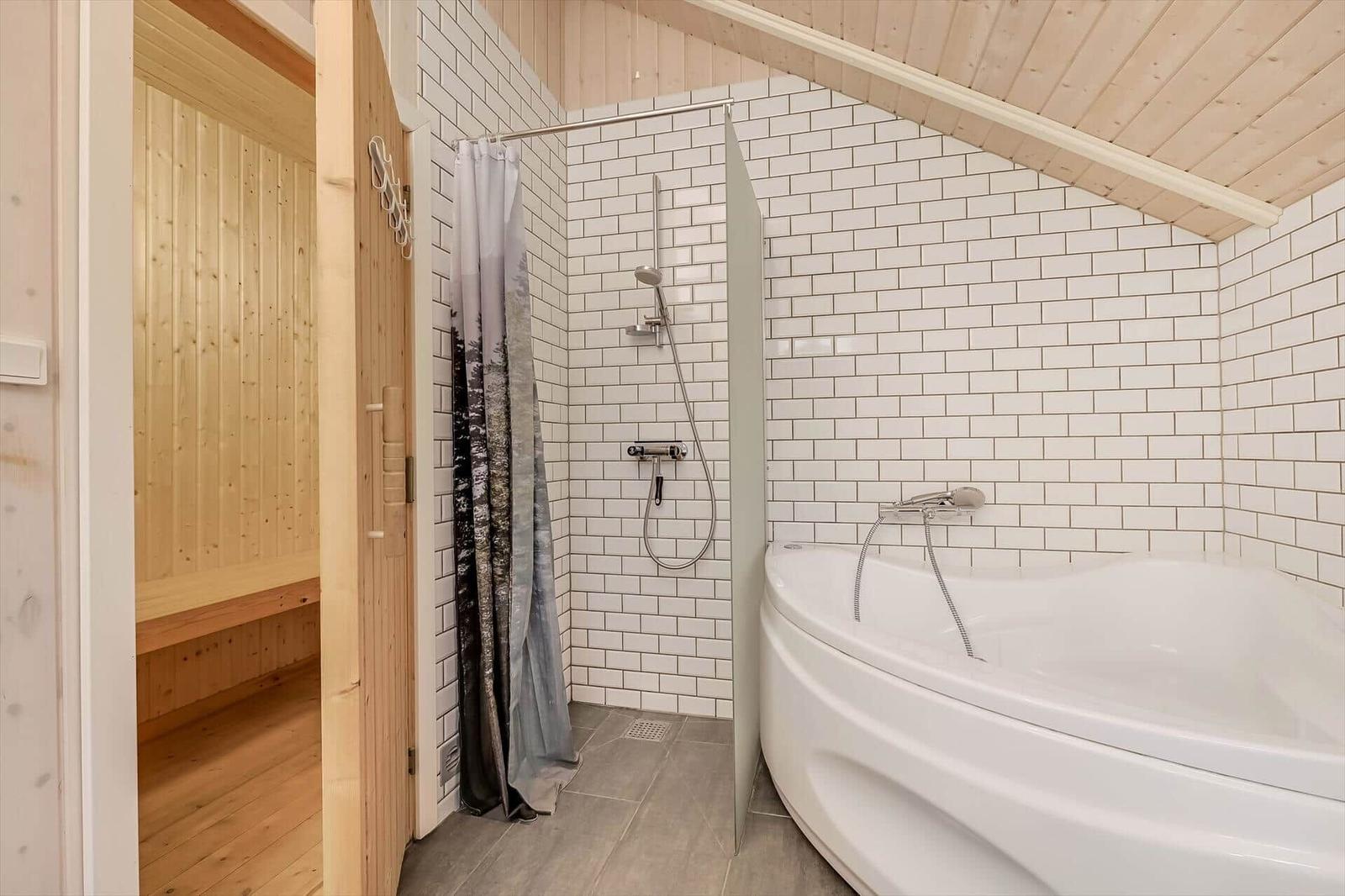 Bad mit Badewanne und Dusche, daneben Sauna mit Holzwand und -boden.