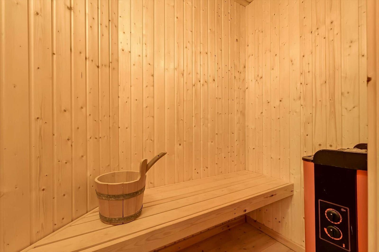 Sauna mit Holzwand, Sitzbank und Holzbucket mit Löffel.