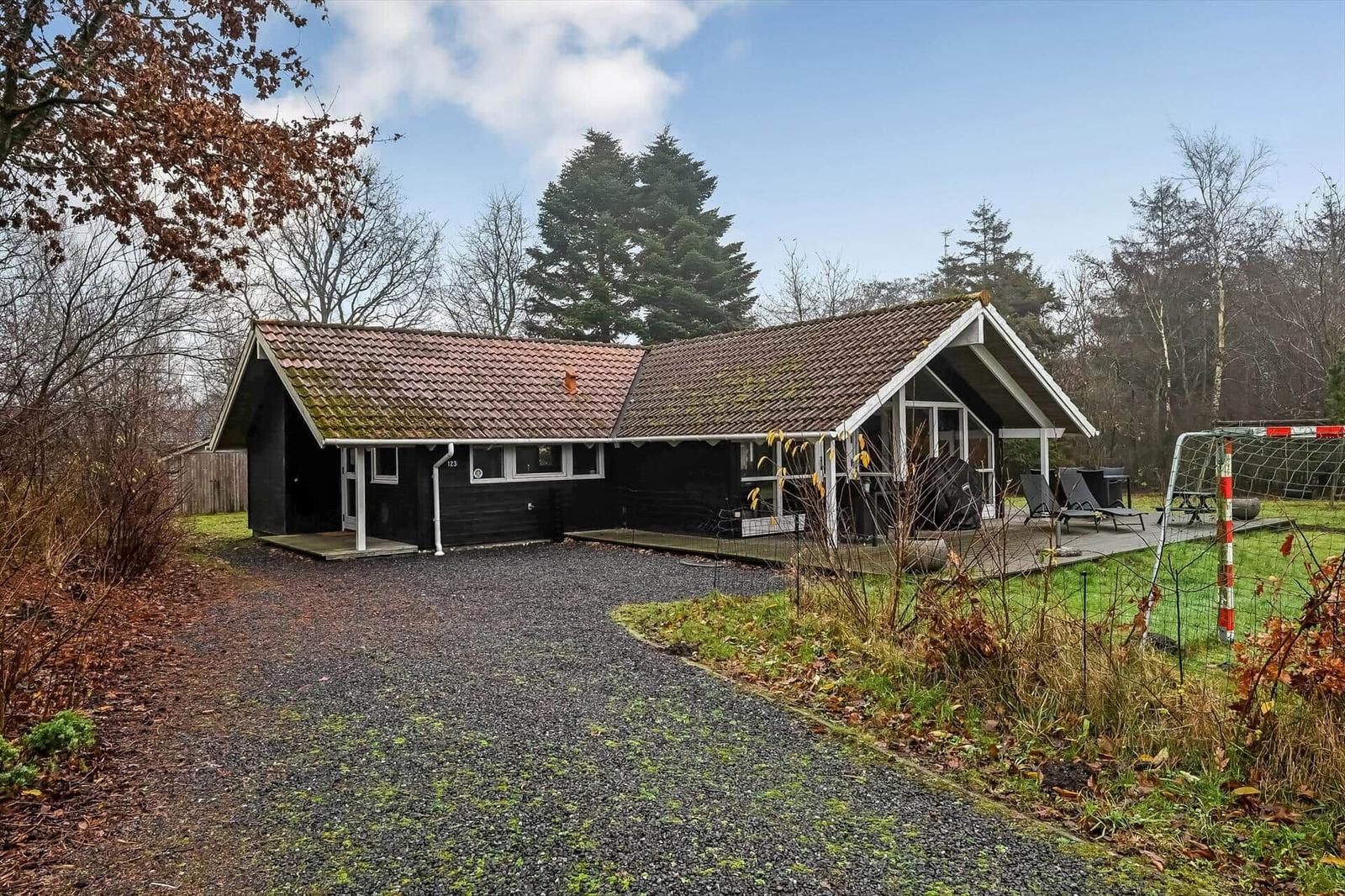 Schwarzes Holzhaus mit Terrasse, Garten und Fußballtor. Gravelweg führt zum Eingang.