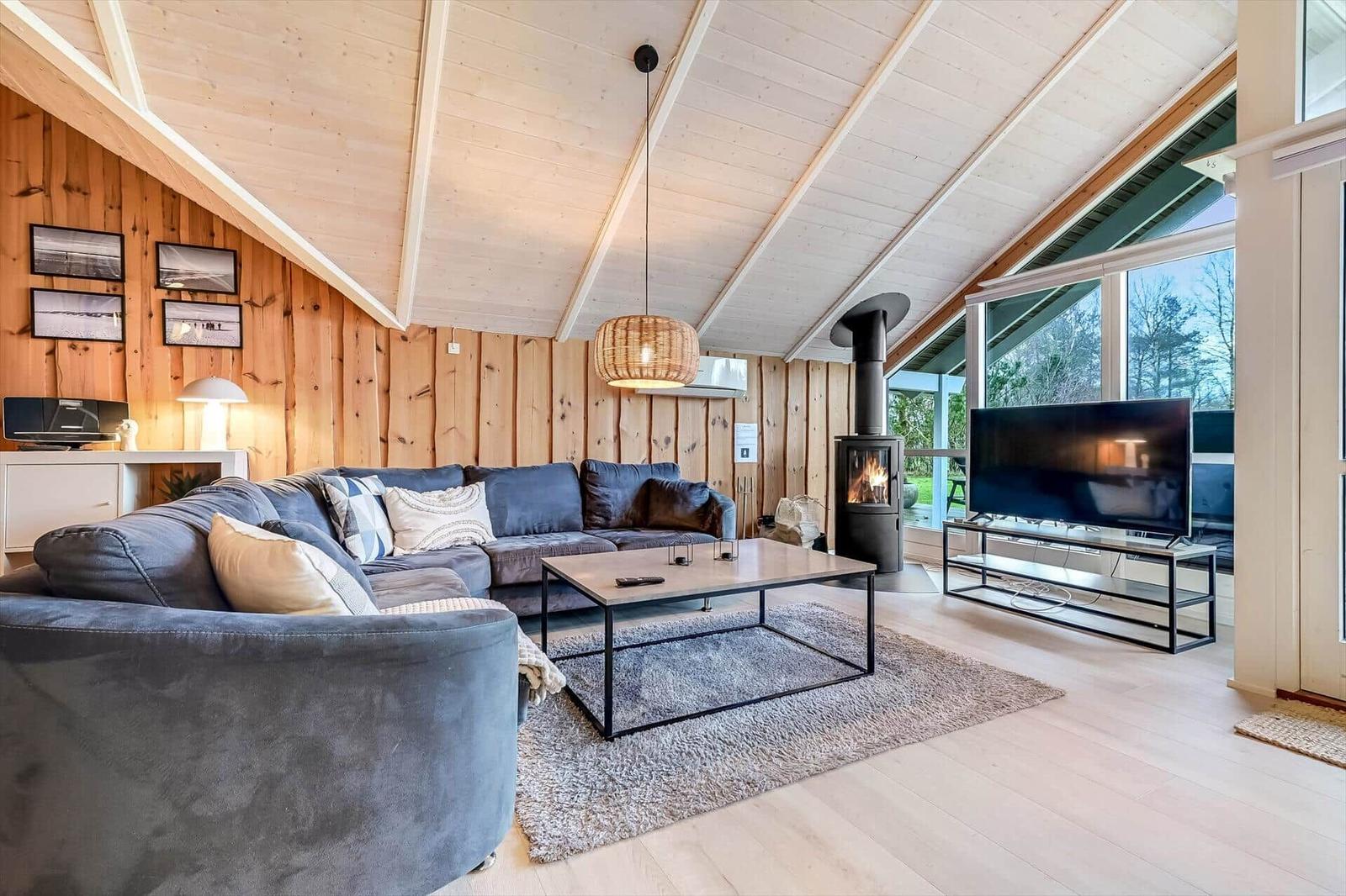 Wohnzimmer mit Sofa, Kamin und Fernseher. Holzwände und hohes Dach.