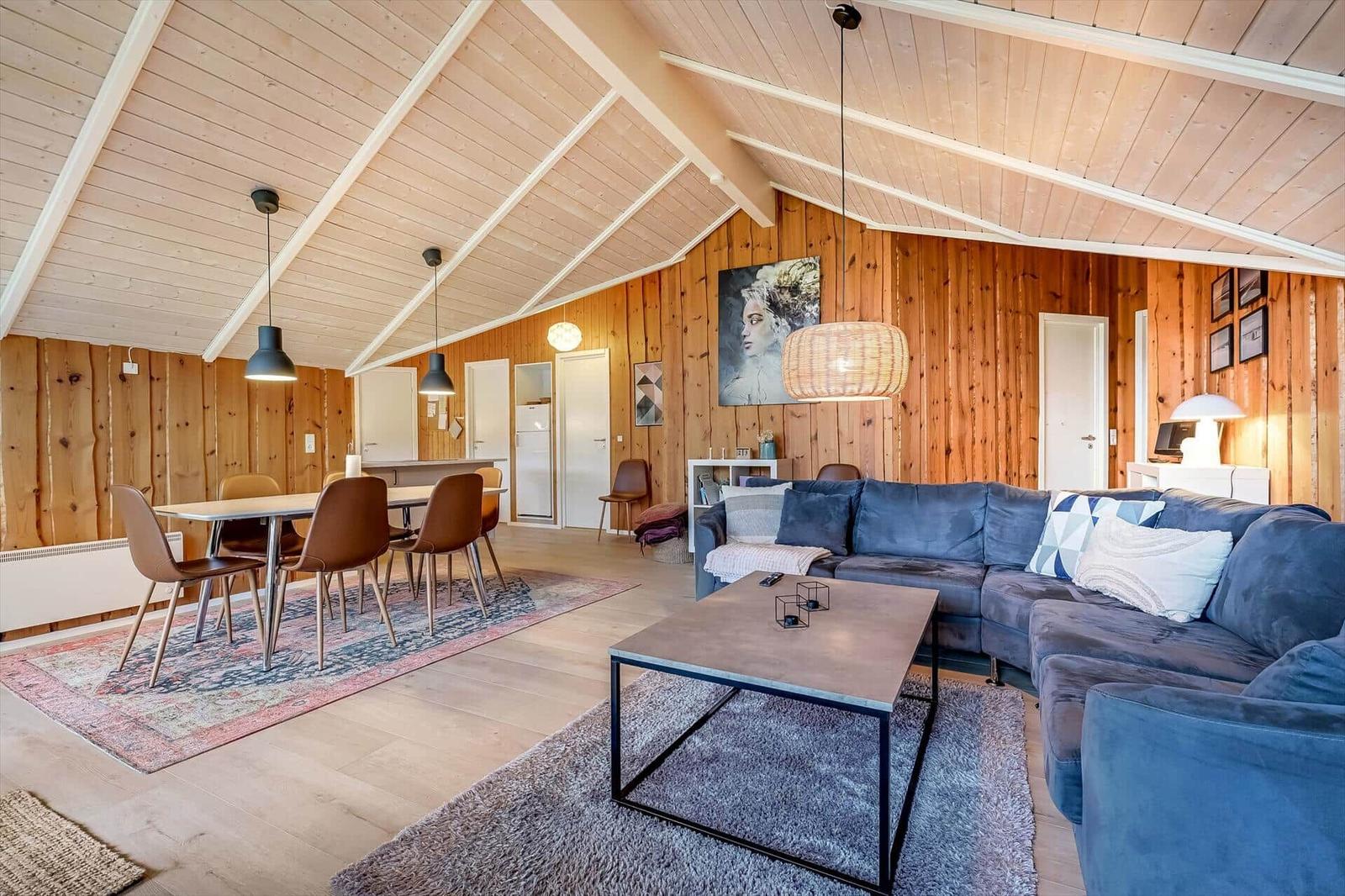 Wohn- und Essbereich mit Holzwänden, Sofa und Tisch. Decke mit Holzbalken.