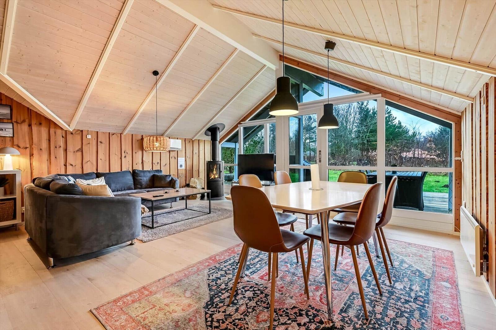 Wohn- und Essbereich mit Holzdecke, Sofa, Esstisch und Blick auf Garten.