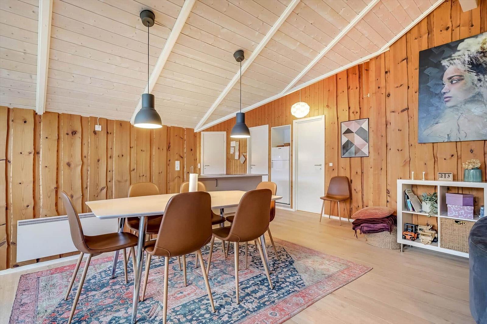 Essbereich mit Tisch, Stühlen und Teppich. Holzwände und Decke. Kunst an der Wand.