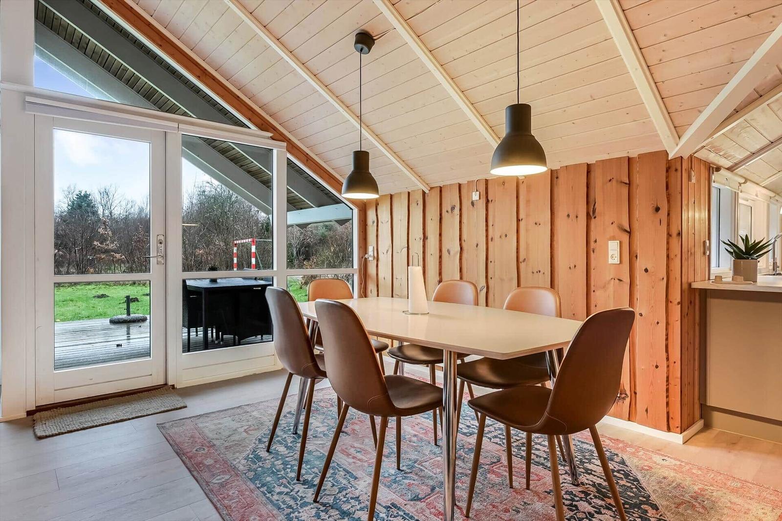 Esszimmer mit Holzwand, Tisch und Stühlen. Durchgang zur Terrasse mit Gartenansicht.