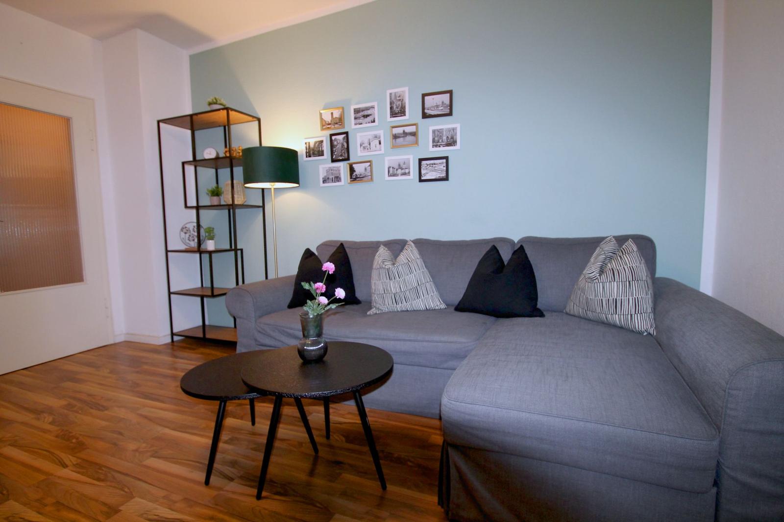 Ein Wohnzimmer mit grauem Sofa, zwei runden Tischen und einer Wand mit Bildern.