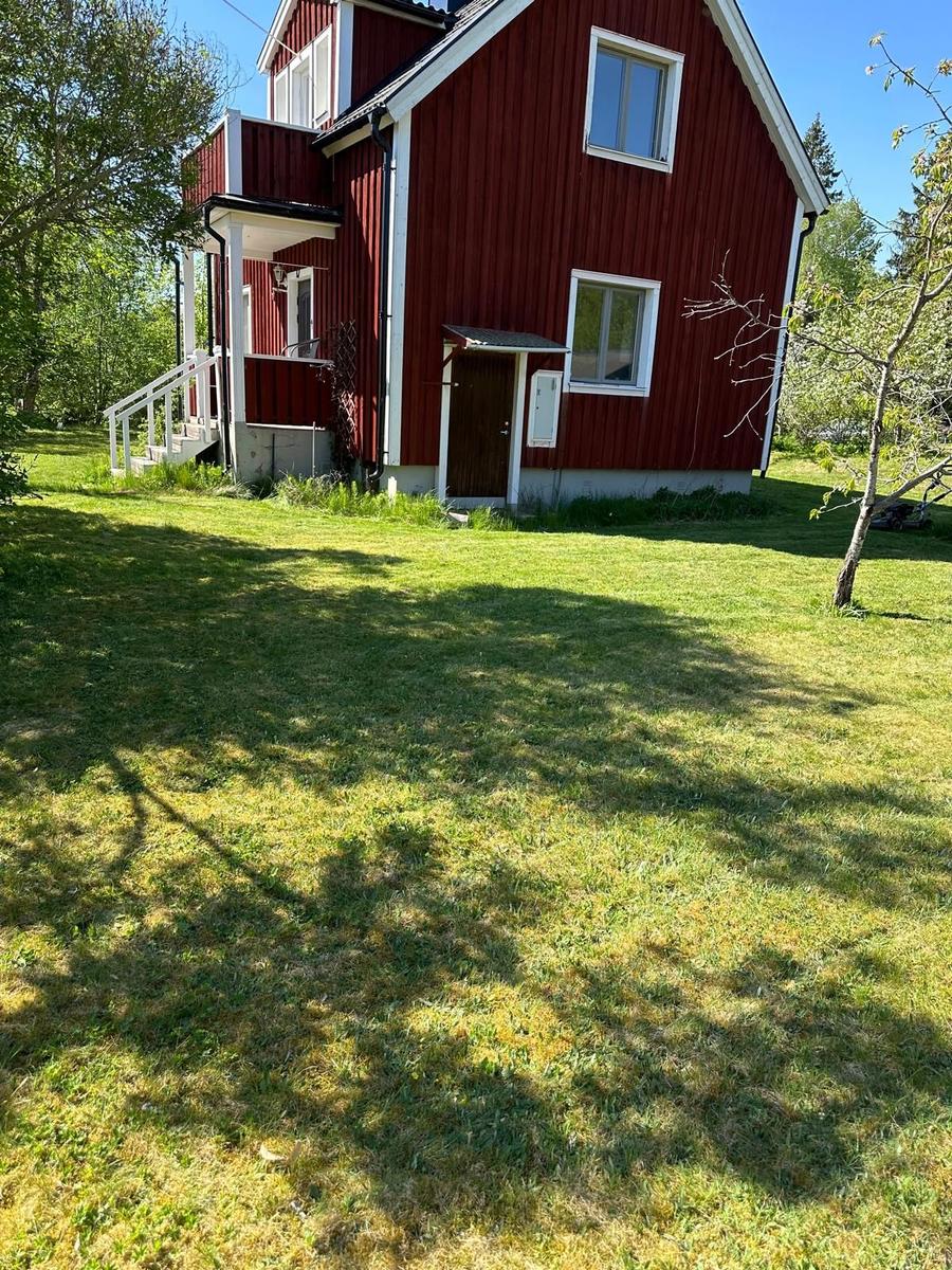 Rotes Holzhaus mit weißem Geländer und Rasenfläche im Freien.