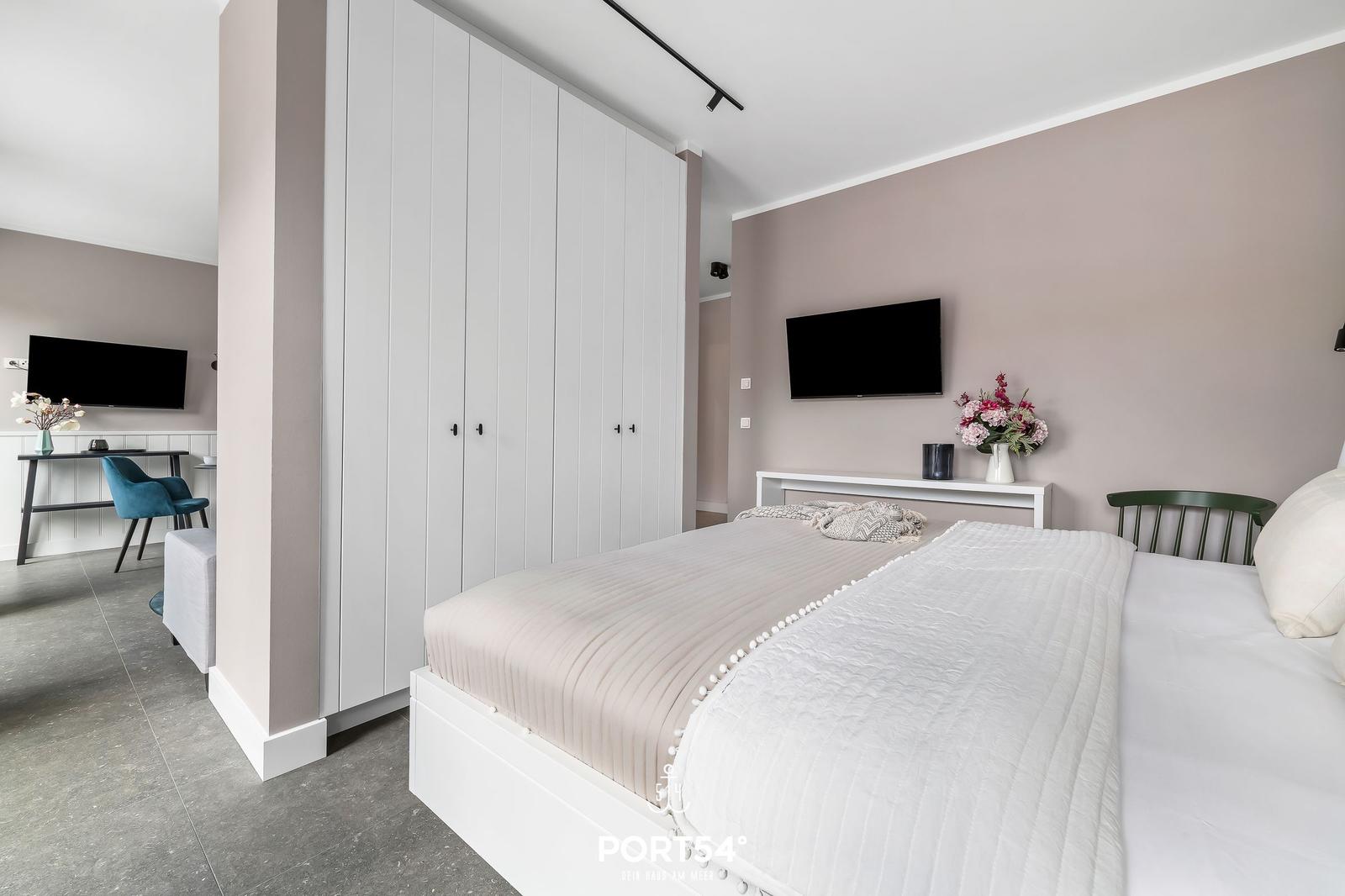 Schlafzimmer mit Bett, Kleiderschrank und Fernseher. Arbeitsplatz im Hintergrund.