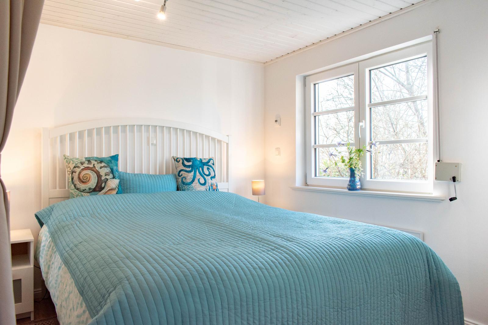 Schlafzimmer mit Bett, Fenster und Blumen