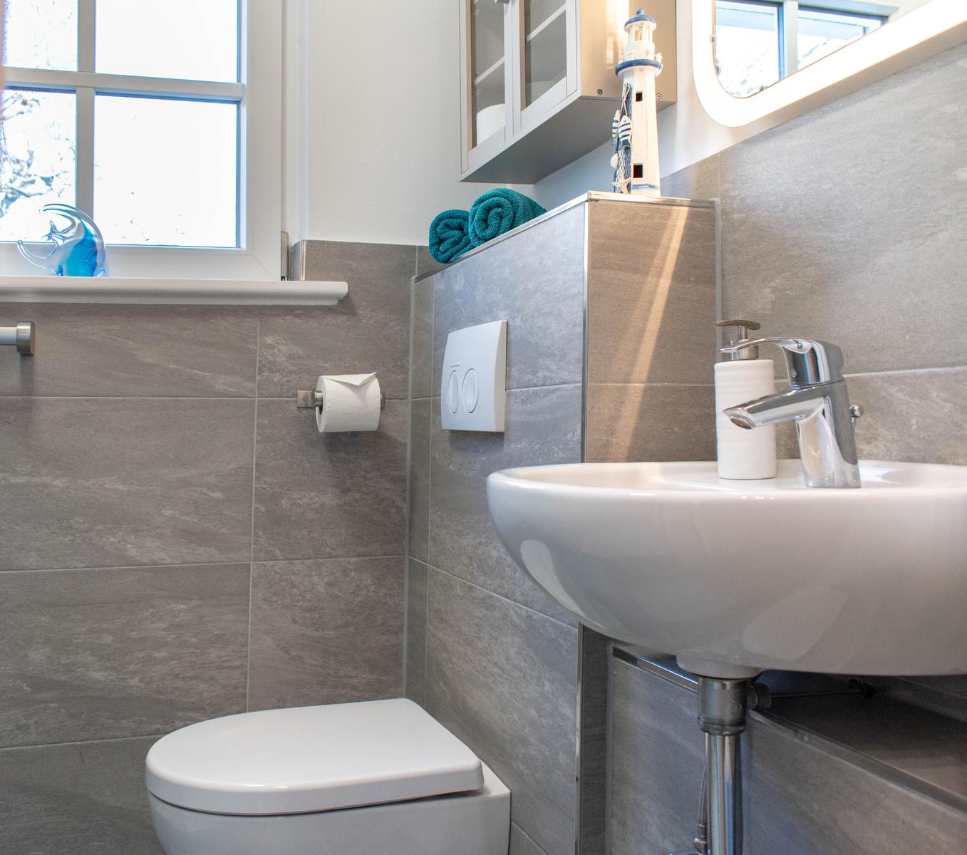 Badezimmer mit Waschbecken, Toilette und Fenster. Auf dem Waschtisch liegen Handtücher.