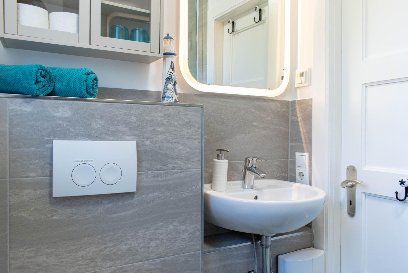 Badezimmer mit Waschbecken, Spiegel und Handtuch. Wandverkleidung grau, Tür weiß.