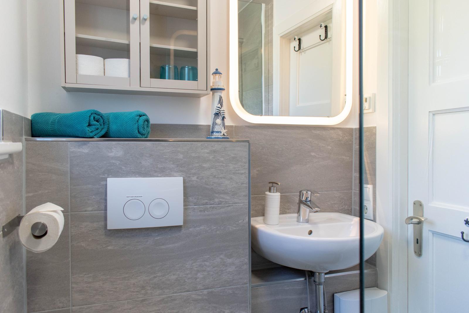 Badezimmer mit Waschbecken, Spiegel, Handtuch und Toilettenpapier