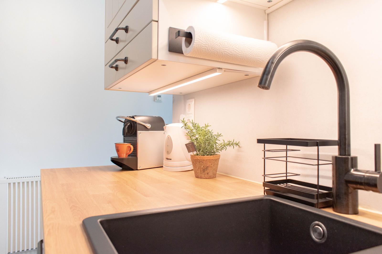 Küche mit Arbeitsplatte, Spüle, Wasserhahn und Küchenutensilien.