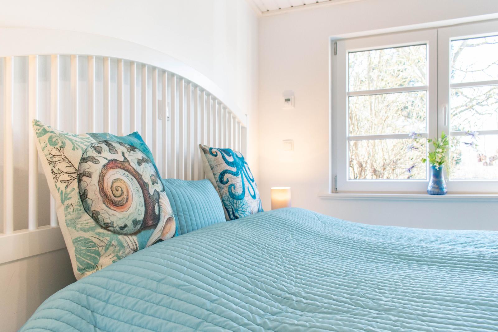 Schlafzimmer mit Bett, Kissen und Fenster. Auf dem Fensterbrett steht eine Vase.