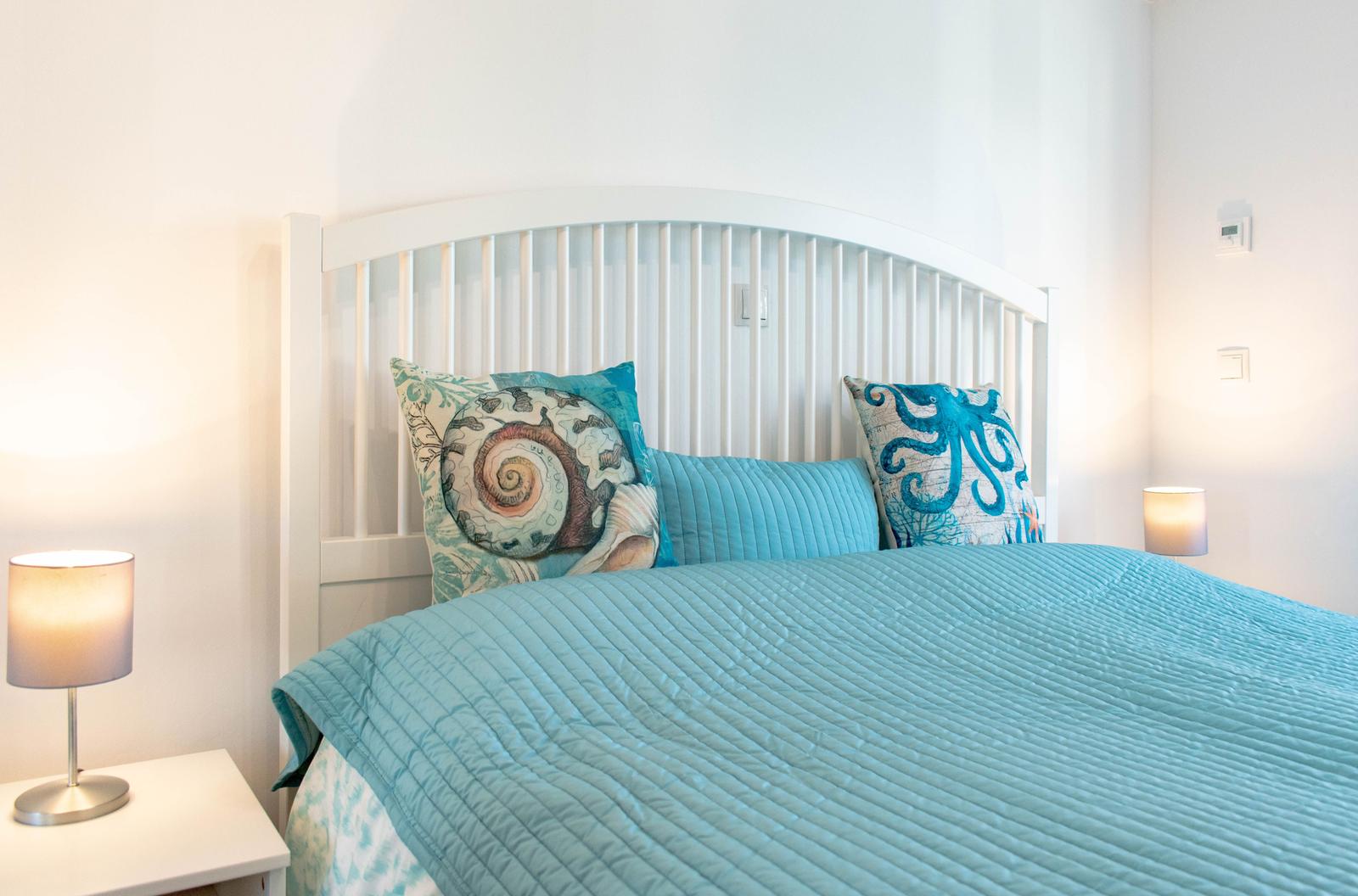 Schlafzimmer mit Bett, Kissen und Nachttisch mit Lampe.