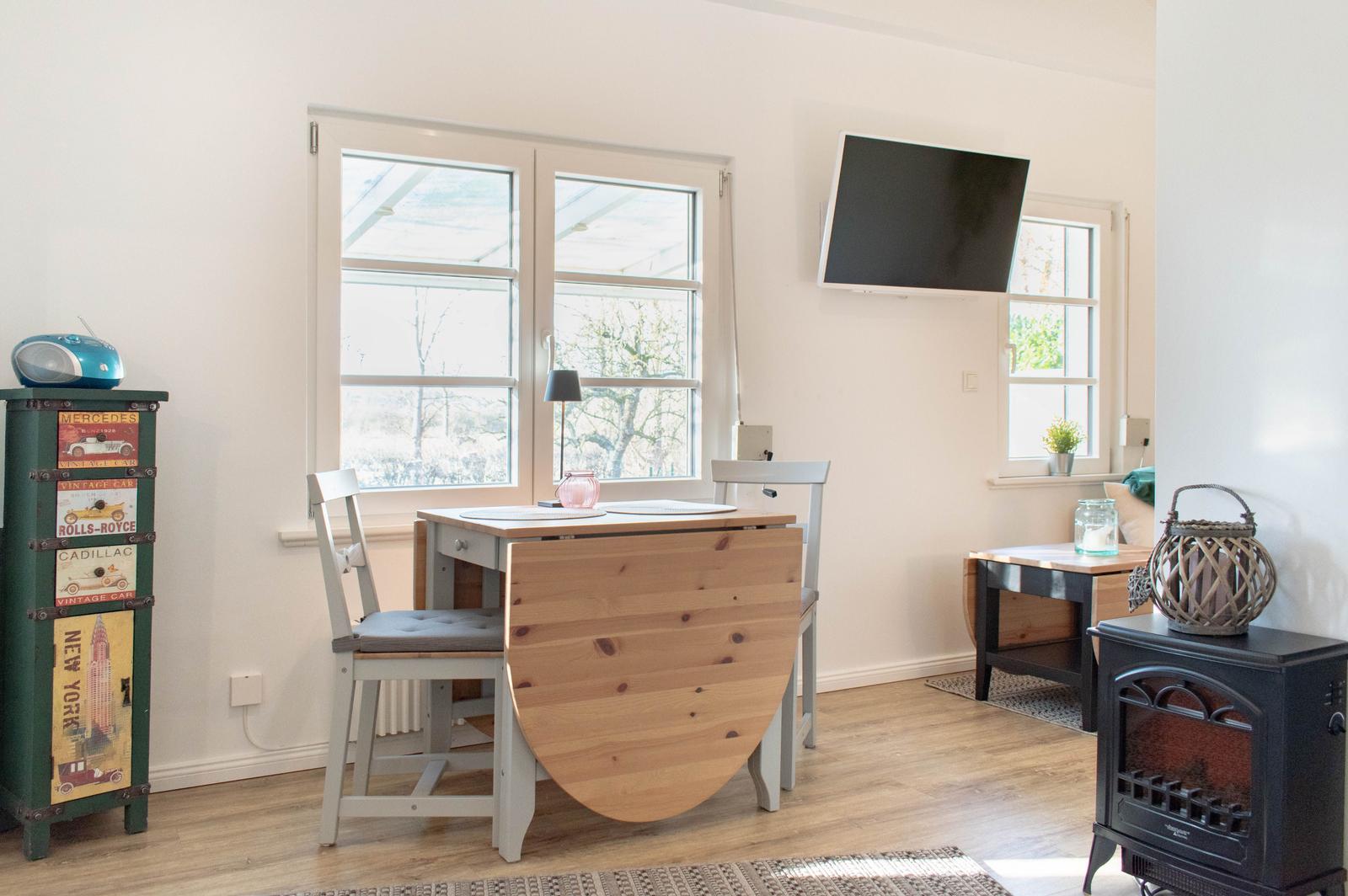 Essbereich mit Tisch, Stühlen und TV an der Wand. Fenster und Holzboden.