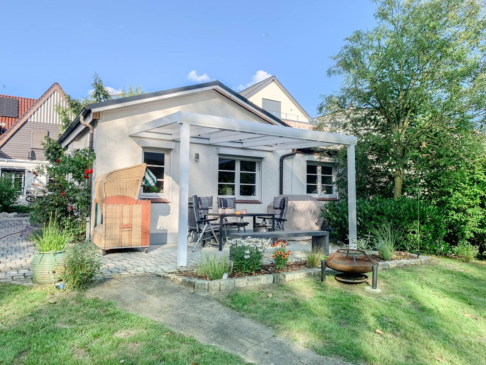 Hinterhof mit Terrasse, Sitzgelegenheiten und Grillplatz. Grünflächen und Pflanzen umgeben das Haus.